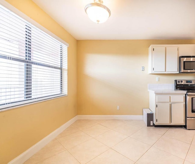 kitchen with light tile patterned floors, baseboards, white cabinets, tile countertops, and appliances with stainless steel finishes