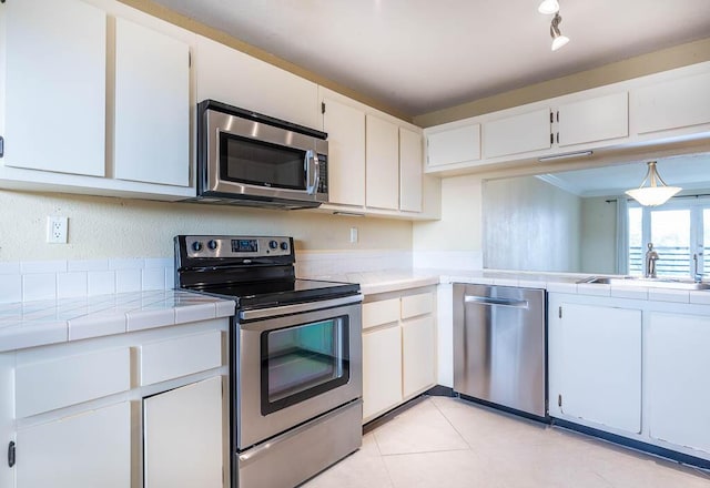 kitchen featuring light tile patterned floors, stainless steel appliances, tile counters, white cabinetry, and a sink