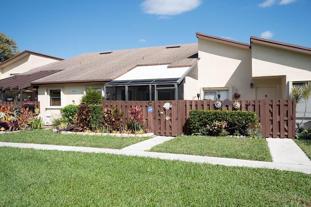 view of front facade featuring a front yard, roof with shingles, fence, and stucco siding