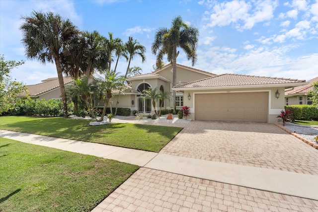 mediterranean / spanish home with a tile roof, an attached garage, decorative driveway, a front yard, and stucco siding