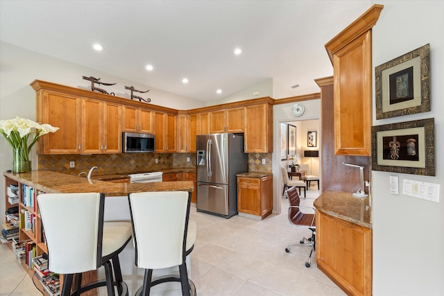 kitchen with stainless steel appliances, a peninsula, a kitchen breakfast bar, brown cabinets, and decorative backsplash