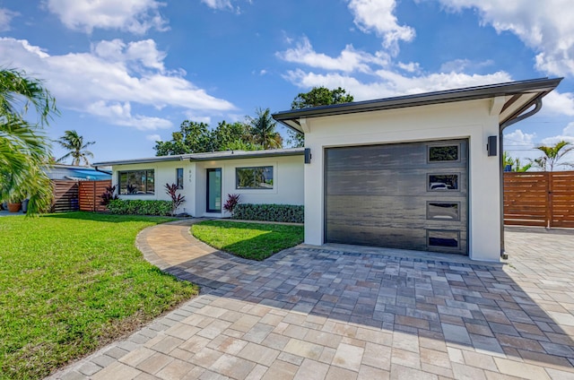 view of front facade with decorative driveway, stucco siding, fence, a garage, and a front lawn