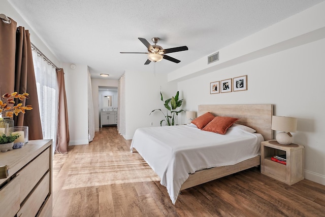 bedroom with visible vents, ensuite bathroom, a textured ceiling, light wood-type flooring, and baseboards