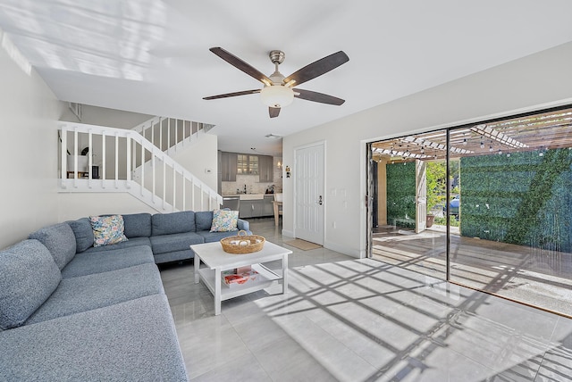 living area with ceiling fan, stairway, and baseboards