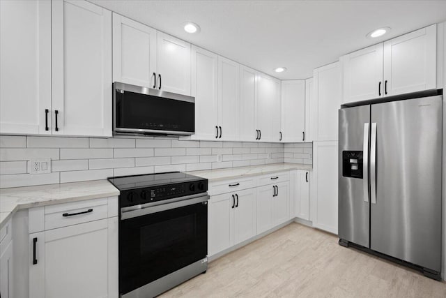 kitchen featuring light wood finished floors, stainless steel appliances, backsplash, white cabinets, and light stone countertops