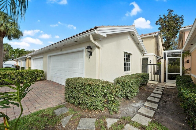 view of side of home featuring a garage, driveway, a tiled roof, and stucco siding