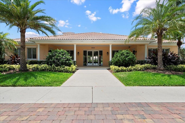 view of front of home with french doors, a tiled roof, a front lawn, and stucco siding