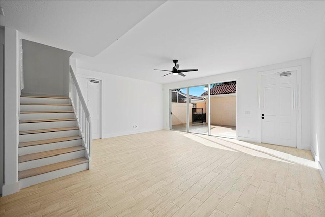 unfurnished living room with light wood-style flooring, ceiling fan, stairway, and baseboards