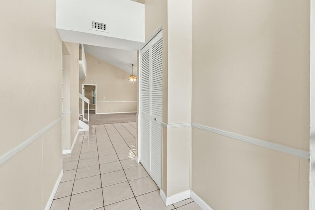 hallway featuring lofted ceiling, light tile patterned flooring, visible vents, and stairs