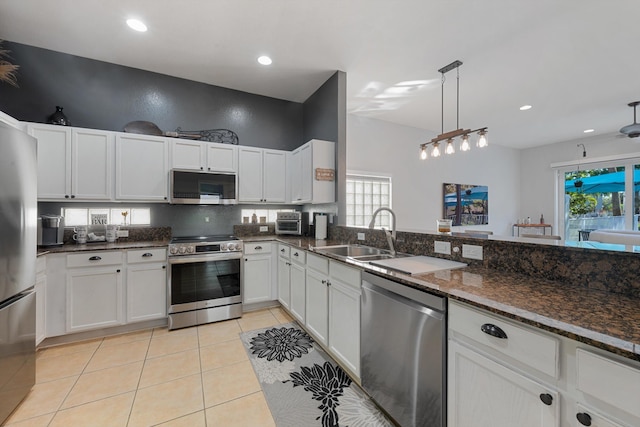 kitchen with decorative light fixtures, light tile patterned floors, appliances with stainless steel finishes, a sink, and dark stone countertops