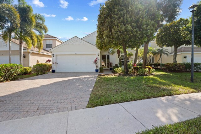 view of front facade featuring a front yard, decorative driveway, an attached garage, and stucco siding