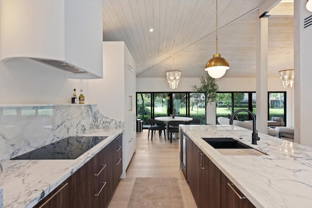 kitchen featuring custom range hood, decorative light fixtures, black electric cooktop, dark brown cabinets, and a sink