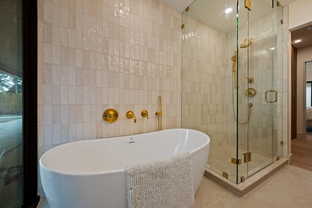 ensuite bathroom with tile patterned floors, ensuite bathroom, a freestanding bath, a shower stall, and tile walls