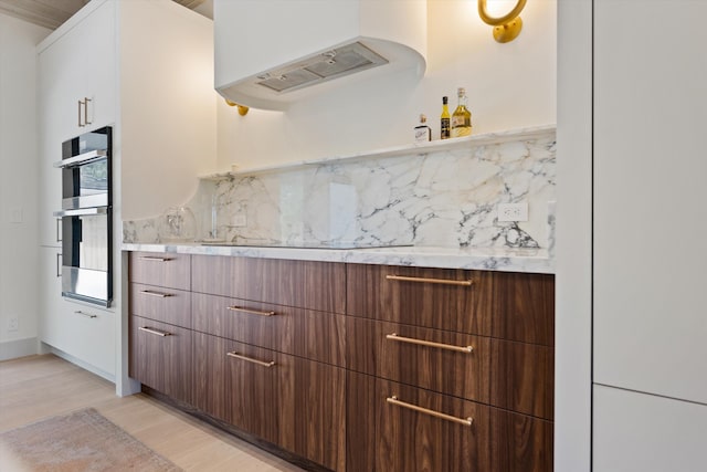 kitchen featuring light countertops, double oven, white cabinetry, premium range hood, and black electric cooktop