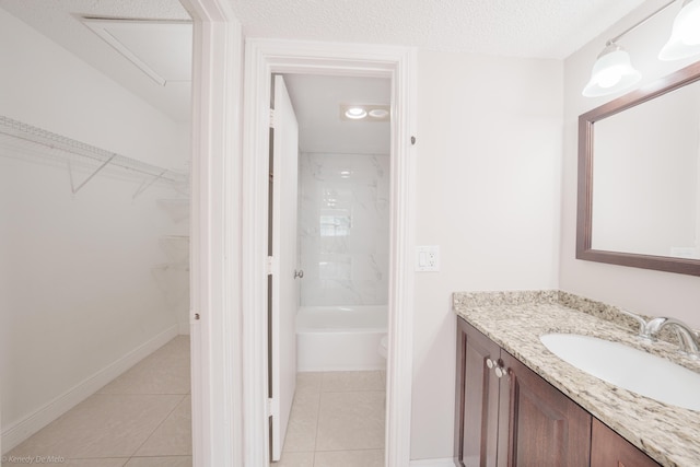 bathroom featuring a walk in closet, vanity, a textured ceiling, tile patterned flooring, and baseboards