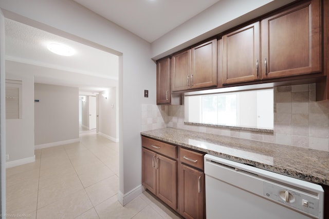 kitchen with light tile patterned floors, tasteful backsplash, baseboards, dishwasher, and light stone countertops