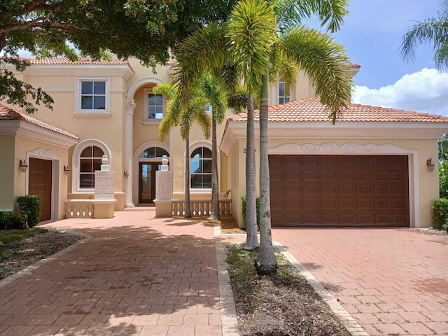 mediterranean / spanish-style home with a tiled roof, decorative driveway, an attached garage, and stucco siding