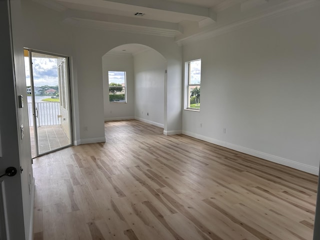 empty room featuring arched walkways, crown molding, light wood finished floors, visible vents, and baseboards