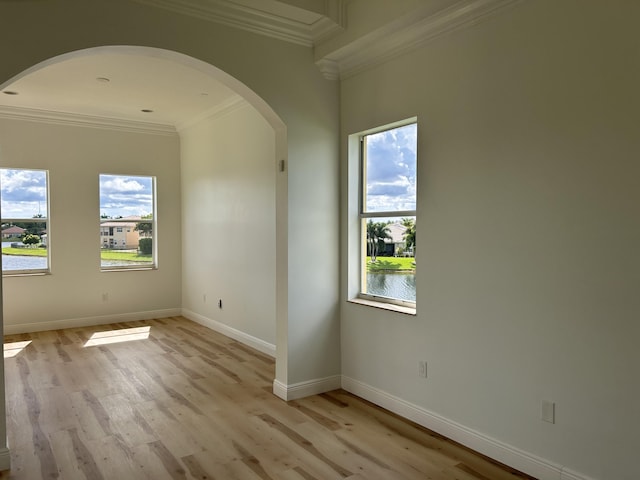 unfurnished room featuring light wood-style floors, arched walkways, a healthy amount of sunlight, and baseboards