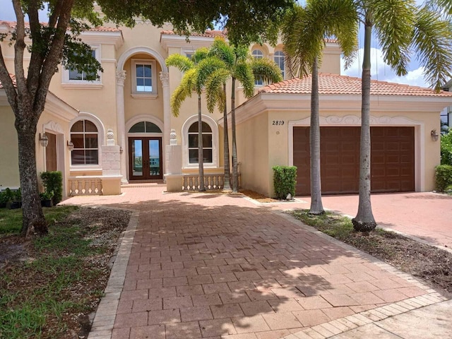 mediterranean / spanish-style house featuring a garage, french doors, a tile roof, and stucco siding