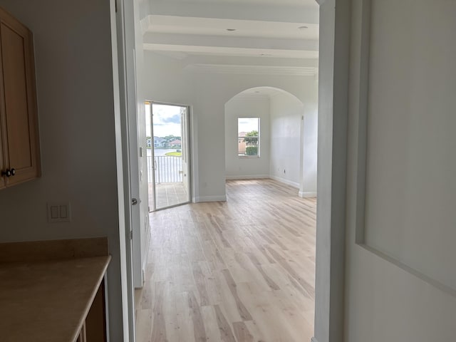 hallway featuring light wood-style floors, baseboards, and arched walkways