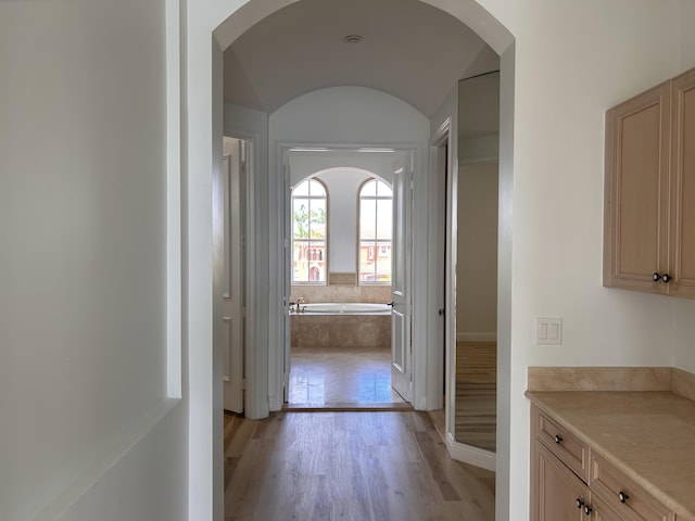 hall with arched walkways, light wood-type flooring, and baseboards