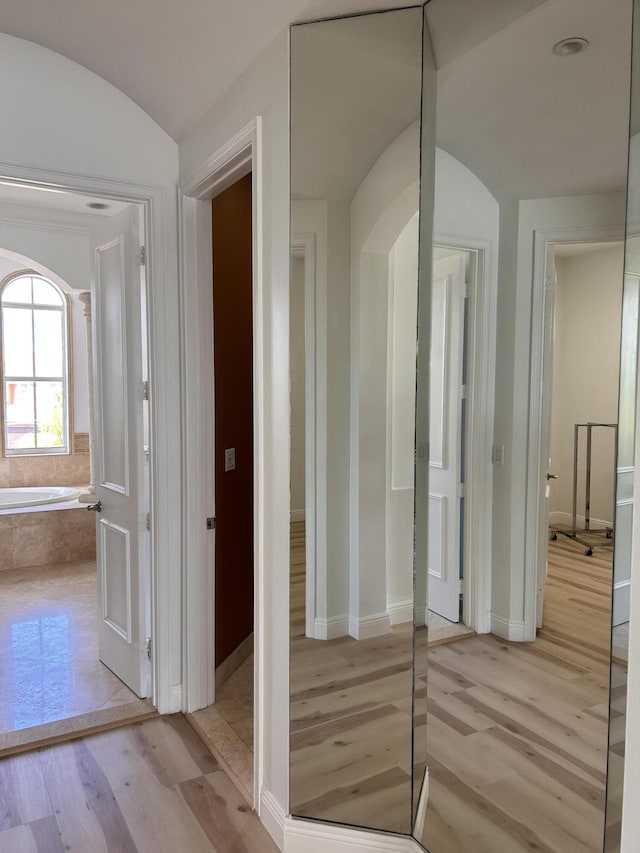 corridor featuring baseboards, arched walkways, and light wood-style floors