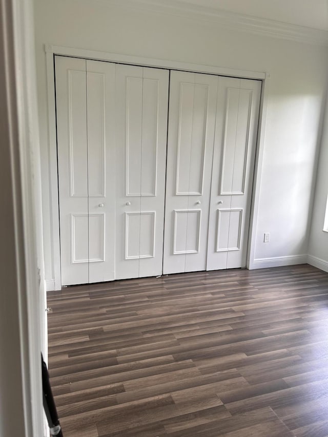 unfurnished bedroom with crown molding, dark wood-type flooring, and a closet