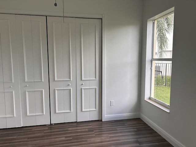 unfurnished bedroom with dark wood-style flooring, a closet, and baseboards