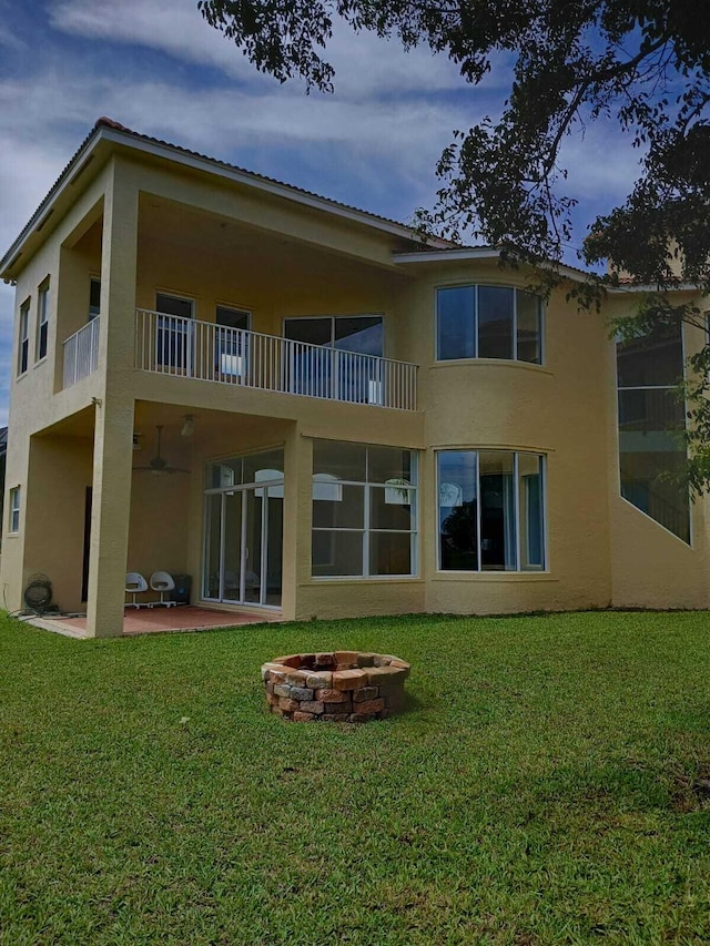 rear view of property featuring an outdoor fire pit, a patio area, a yard, and stucco siding