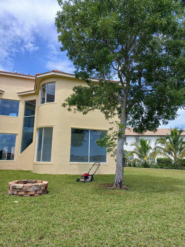 view of side of property with an outdoor fire pit, a yard, and stucco siding