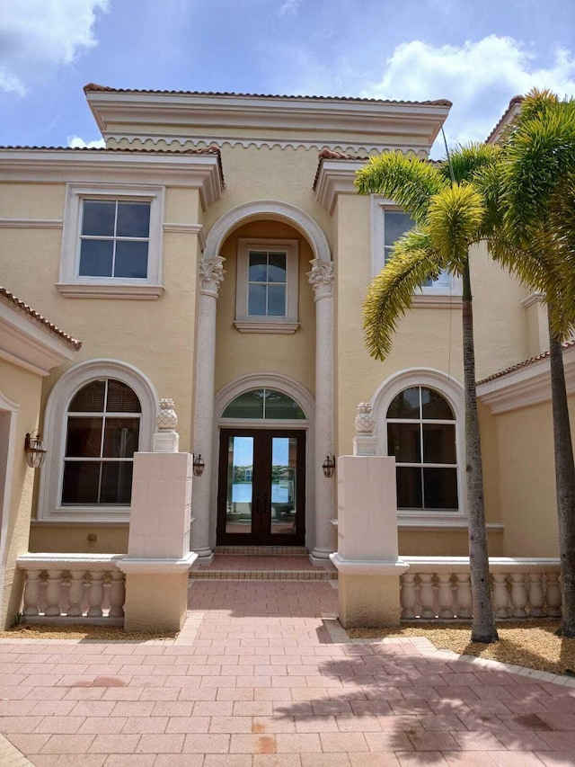 view of exterior entry with french doors, a tiled roof, and stucco siding