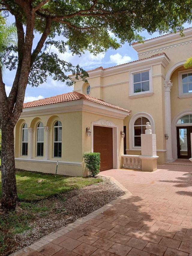 mediterranean / spanish house featuring a garage, decorative driveway, a tile roof, and stucco siding