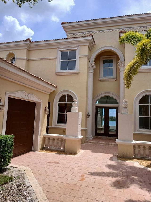 view of exterior entry featuring french doors, stucco siding, a garage, driveway, and a tiled roof