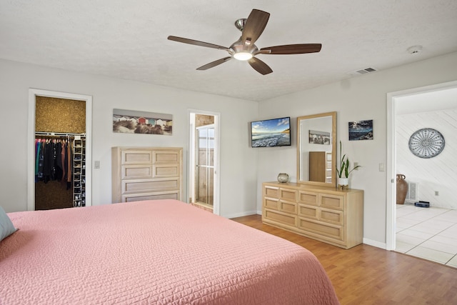 bedroom with visible vents, a spacious closet, a textured ceiling, ensuite bath, and wood finished floors