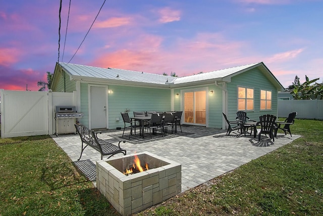 back of house featuring metal roof, a patio, a fire pit, fence, and a gate