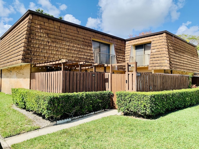 view of side of home featuring a yard, fence, mansard roof, and brick siding