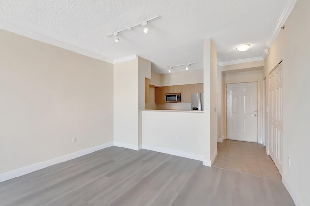 interior space featuring ornamental molding, light wood-style flooring, a textured ceiling, and baseboards