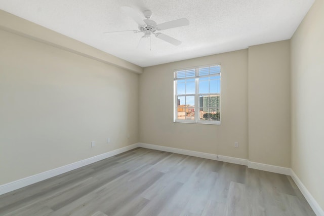 empty room featuring light wood-type flooring, ceiling fan, baseboards, and a textured ceiling