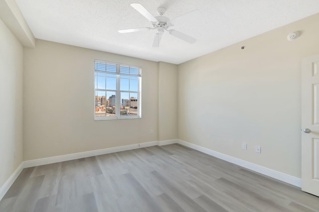 spare room featuring light wood finished floors, ceiling fan, baseboards, and a textured ceiling