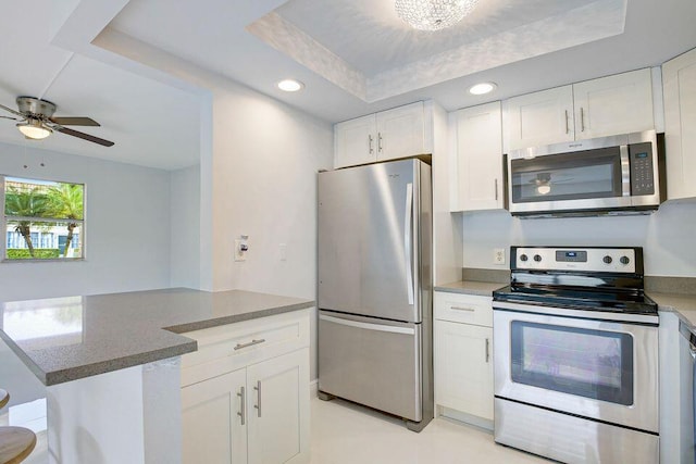 kitchen featuring dark stone counters, white cabinets, a raised ceiling, appliances with stainless steel finishes, and recessed lighting