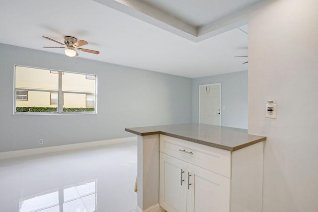 kitchen featuring baseboards, a ceiling fan, dark countertops, a peninsula, and white cabinetry