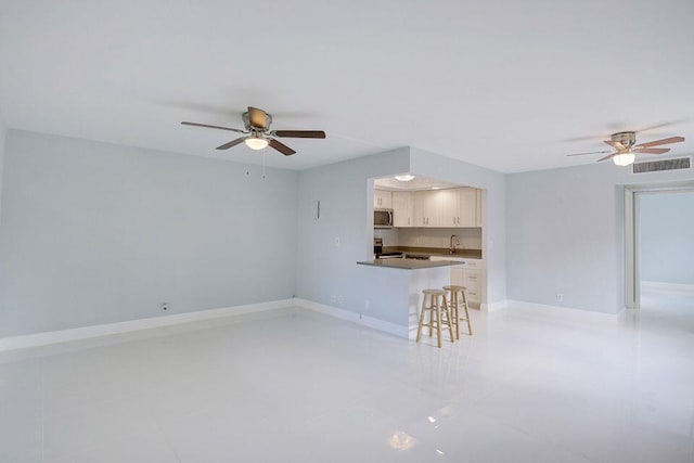 unfurnished living room featuring a ceiling fan, visible vents, and baseboards