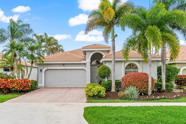 mediterranean / spanish house with a garage, a tiled roof, decorative driveway, and stucco siding