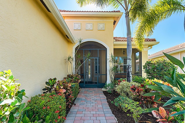 view of exterior entry with french doors, a tile roof, and stucco siding