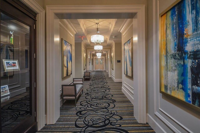 hallway featuring dark colored carpet, an inviting chandelier, and crown molding