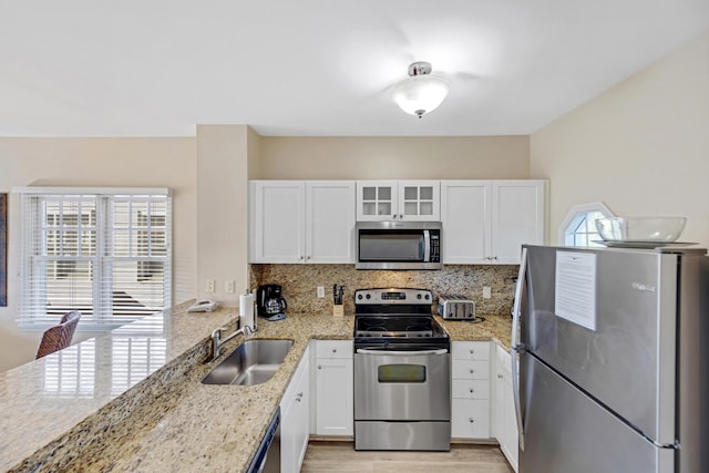 kitchen with light stone counters, stainless steel appliances, a sink, white cabinets, and tasteful backsplash