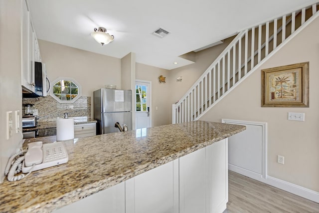 kitchen featuring light stone counters, a peninsula, visible vents, white cabinetry, and freestanding refrigerator