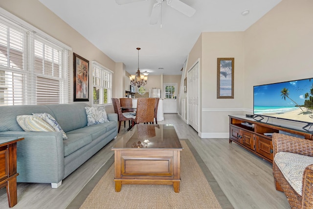 living area with light wood finished floors, baseboards, and ceiling fan with notable chandelier