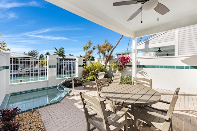 view of patio featuring a hot tub, ceiling fan, fence, and outdoor dining area